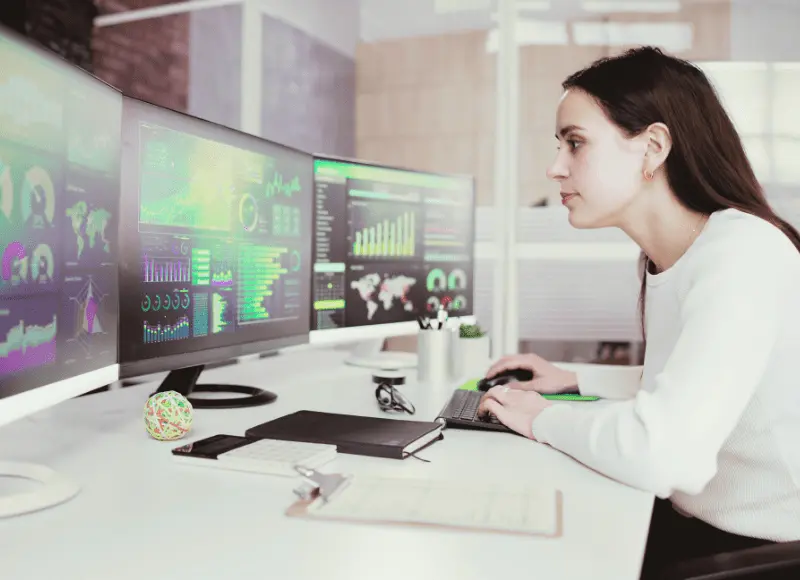 Woman at her desk working on her PC and 3 screens